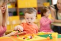 Little kid boy learning to use colorful play clay in kindergarten. Babies group studying in creche