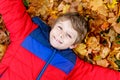 Little kid boy lying in autumn leaves in colorful fashion fall clothing.