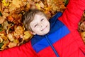 Little kid boy lying in autumn leaves in colorful fashion fall clothing.