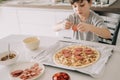 Little kid boy making pizza sitting at the table on the kitchen. Children helping in cooking lifestyle image Royalty Free Stock Photo