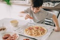 Little kid boy making pizza sitting at the table on the kitchen. Children helping in cooking lifestyle image Royalty Free Stock Photo