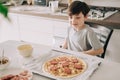 Little kid boy making pizza sitting at the table on the kitchen. Children helping in cooking lifestyle image Royalty Free Stock Photo