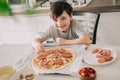 Little kid boy making pizza sitting at the table on the kitchen. Children helping in cooking lifestyle image Royalty Free Stock Photo