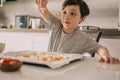 Little kid boy making pizza sitting at the table on the kitchen. Children helping in cooking lifestyle image Royalty Free Stock Photo