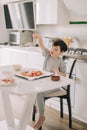 Little kid boy making pizza sitting at the table on the kitchen. Children helping in cooking lifestyle image Royalty Free Stock Photo