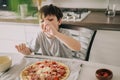 Little kid boy making pizza sitting at the table on the kitchen. Children helping in cooking lifestyle image Royalty Free Stock Photo