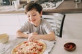 Little kid boy making pizza sitting at the table on the kitchen. Children helping in cooking lifestyle image Royalty Free Stock Photo