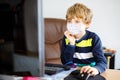 Little kid boy with medical mask learning on computer notebook. Happy healthy child searching information on internet pc