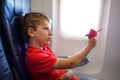 Little kid boy playing with red paper plane during flight on airplane. Child sitting inside aircraft by a window. Family Royalty Free Stock Photo