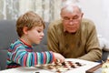 Little kid boy and senior grandfather playing together checkers game