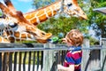 Little kid boy watching and feeding giraffe in zoo Royalty Free Stock Photo