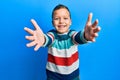 Little kid boy wearing striped sweater looking at the camera smiling with open arms for hug Royalty Free Stock Photo