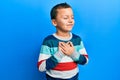 Little kid boy wearing striped sweater smiling with hands on chest, eyes closed with grateful gesture on face Royalty Free Stock Photo