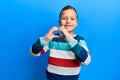 Little kid boy wearing striped sweater smiling in love doing heart symbol shape with hands Royalty Free Stock Photo