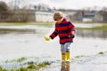 Little kid boy wearing yellow rain boots and walking and jumping into puddle on warm sunny spring day. Happy child in Royalty Free Stock Photo