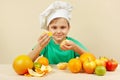 Little kid in chefs hat peeling fresh orange at table with fruits Royalty Free Stock Photo