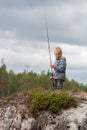 Little kid fisherman holding fishing rod while fly fishing on river in forest. Boy child catches fish with spinning rod, casting