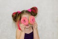 A little kid girl dabbles and plays with two fresh donuts before eating. A child holds donuts near his eyes and looks through the Royalty Free Stock Photo