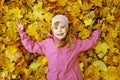 Little kid girl lying on colorful fall leaves background in autumn park, top view. Child girl is dressed in pink hat and jacket