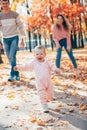 Little kid girl runs in autumnal couple and plays with parents. toddler runs away on autumn yellow leaves from mother Royalty Free Stock Photo