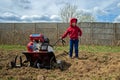 Little kid girl in spring with garden cultivator in field outdoors. Funny toddler pose with working in garden