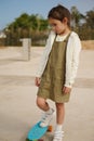 Little kid girl standing on skateboard on one leg, expressing sad emotions having difficulties on learning skateboarding Royalty Free Stock Photo