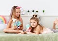 Little kid girls sisters in home clothing spend time together playing with their favorite dolls in bed at home