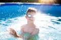 Little kid in goggles splashing in swimming pool
