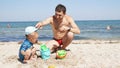 Little kid and his careful father on the beach playing with pails and sand Royalty Free Stock Photo