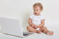 Little kid with laptop sitting on floor with opened mouth and looking directly at lap top screen, has concentrated look, dresses Royalty Free Stock Photo