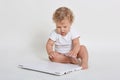 Little kid with laptop sitting on ground, closed laptop computer with great interest, curious infant plays barefoot with notebook