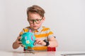 little kid open piggy bank. Blond little boy putting money on a moneybox. Portrait of a stylish kid in green glasses