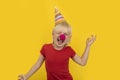 Little kid with party hat and red nose clown having fun. Portrait on yellow background. Party for children Royalty Free Stock Photo
