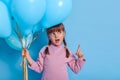 Little kid with pigtails bunch of balloon and pointing aside with fore finger, keeps mouth opened, looks aside with interest,