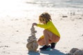 Little kid play with pyramid stones balance on the sand of the beach. Kid with stack of stones on sand near sea. Child Royalty Free Stock Photo