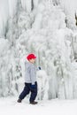 Seasonal winter mood, attractive frozen waterfall, iciles, young boy in red cap plays. Royalty Free Stock Photo