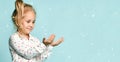 Little blonde kid with ponytail, in shirt with hearts print. She smiling, holding something posing on green background. Close up Royalty Free Stock Photo