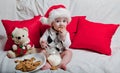 A little kid in a red cap eats a cookies and milk. Christmas photography of a baby in a red cap. New Year holidays and Christmas