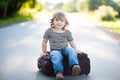 Little kid sitting on a suitcase outdoors, ready for the journey