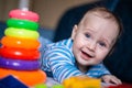 A little kid in a striped suit is lying on his tummy, next to him a children's pyramid and toys. Royalty Free Stock Photo