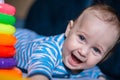 A little kid in a striped suit is lying on his tummy, next to him a children's pyramid and toys. Royalty Free Stock Photo