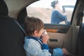 Little kid in sweater drinking cup of tea inside car with mother woman calling phone outside during travel trip stop Royalty Free Stock Photo