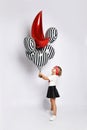 Little kid in t-shirt, red headband, black skirt and sneakers. Holding balloons, posing sideways isolated on white. Full length Royalty Free Stock Photo