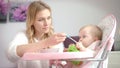 Kid with toy eating pureed food from baby bowl. Woman feeding baby in chair