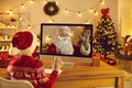 Little kid video calling Father Christmas and waving hand at screen sitting in cozy room at home Royalty Free Stock Photo