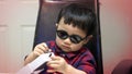 Little Kid wearing sunglasses and casual suit is concentrate with stuff in white boxset.