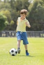 Little kid 7 or 8 years old enjoying happy playing football soccer at grass city park field running and kicking the ball excited i Royalty Free Stock Photo