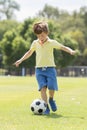 Little kid 7 or 8 years old enjoying happy playing football soccer at grass city park field running and kicking the ball excited i Royalty Free Stock Photo