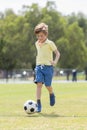 Little kid 7 or 8 years old enjoying happy playing football soccer at grass city park field running and kicking the ball excited i Royalty Free Stock Photo