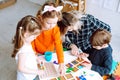 Little kids with educator folding colorful details of constructor on desk in playroom from above view. Interesting game